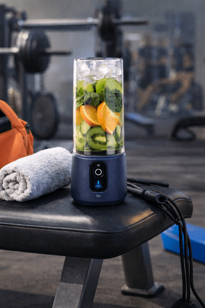 Cordless portable blender blending fruit and greens on a gym bench with workout gear nearby