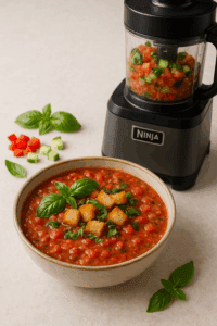 Chunky gazpacho in a bowl with basil and croutons next to Ninja Mega Kitchen System