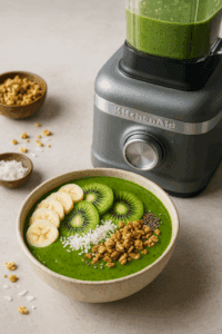 Green smoothie bowl topped with fruit and granola next to KitchenAid K400