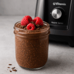 Glass jar filled with chocolate chia pudding topped with berries beside a Vitamix Ascent blender