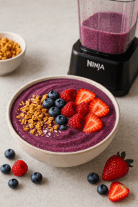 Thick berry smoothie bowl topped with granola and fresh fruit next to a Ninja BN751 blender