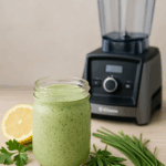 Green Goddess dressing in a small bowl next to fresh herbs and a Vitamix blender