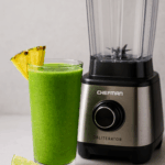 Bright green smoothie with pineapple and lime in a clear glass beside the Chefman Obliterator Blender